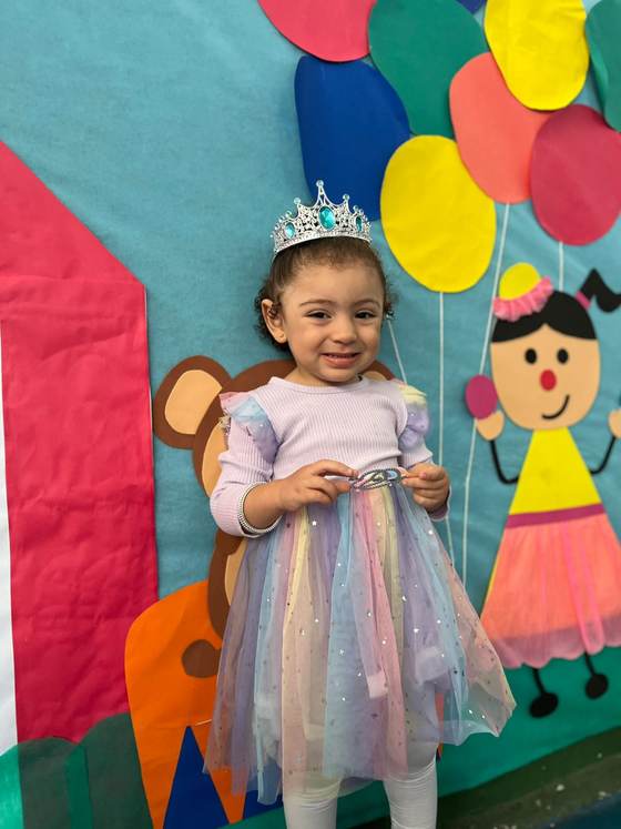 Aluna da Creche Escola Santa Beatriz fantasiada de princesa no Dia das Crianças, em frente ao painel decorado