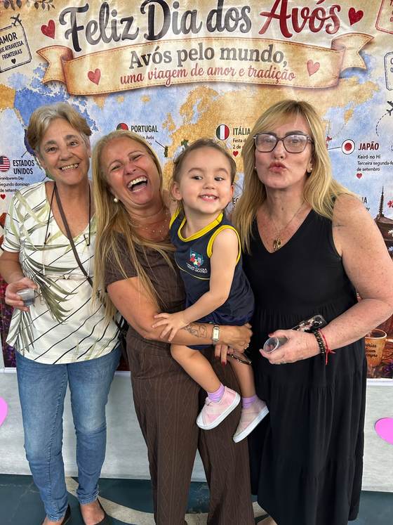 Avós com a neta no colo em frente ao painel Avós pelo mundo, da Creche Escola Santa Beatriz