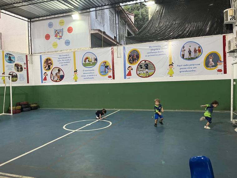 Crianças correndo atrás da bola durante a aula de futsal na quadra coberta da Creche Escola Santa Beatriz